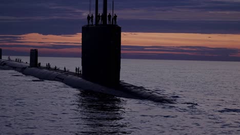 silhouetted submarine at sunset with crew on deck, captured from a low angle