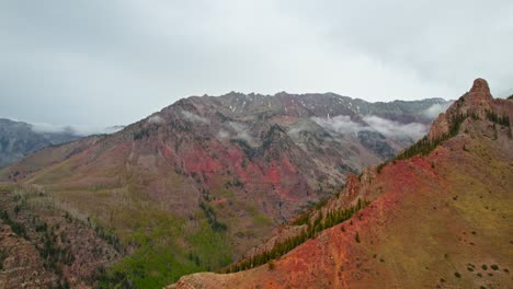 Aerial-Drone-Footage-Beautiful-Mountain-Environment-During-Cloudy-Rainy-Day-Showing-Deep-Alpine-Valley-With-Pine-Trees-And-Red-Mountain-Rock-Terrain