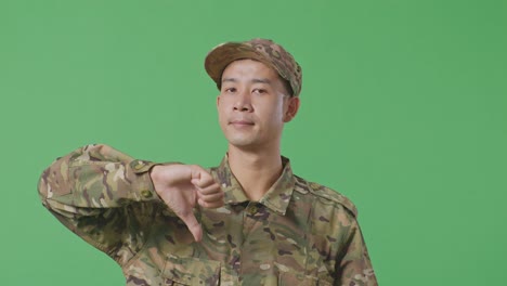 close up of asian man soldier showing thumbs down gesture to camera while standing in the green screen background studio