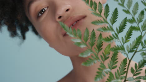 close up portrait beautiful mixed race woman touching face with leaf caressing smooth healthy skin complexion enjoying playful natural beauty on blue background skincare concept