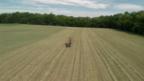 aerial drone shot flying orbit over tractor and farmers harvesting in hay field