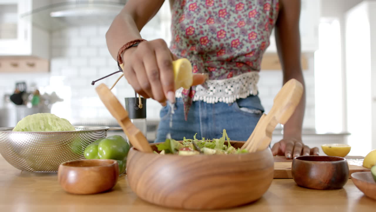 African American young woman preparing salad in kitchen, at home