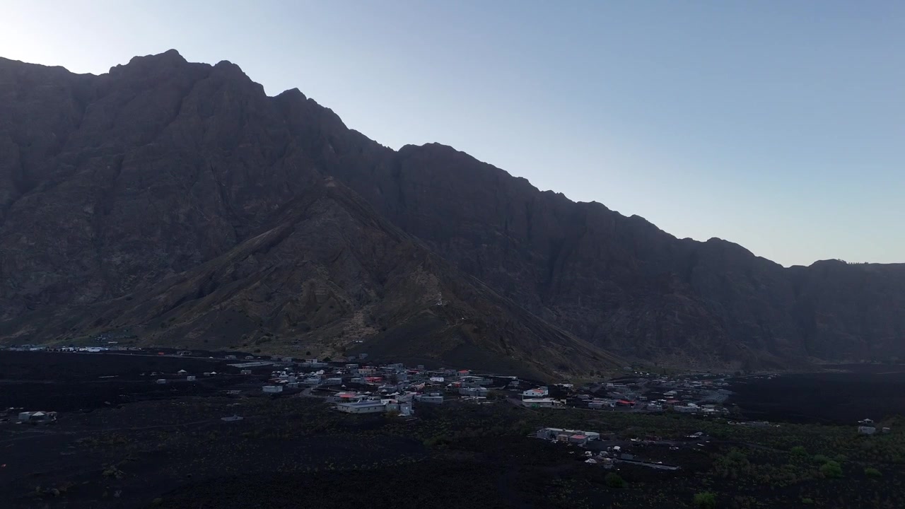カーボベルデ、フォゴ島の夕暮れ時、黒い火山性溶岩原に位置する劇的なボルデイラ断崖と人里離れたチャ・ダス・カルデイラス村の広角空撮。