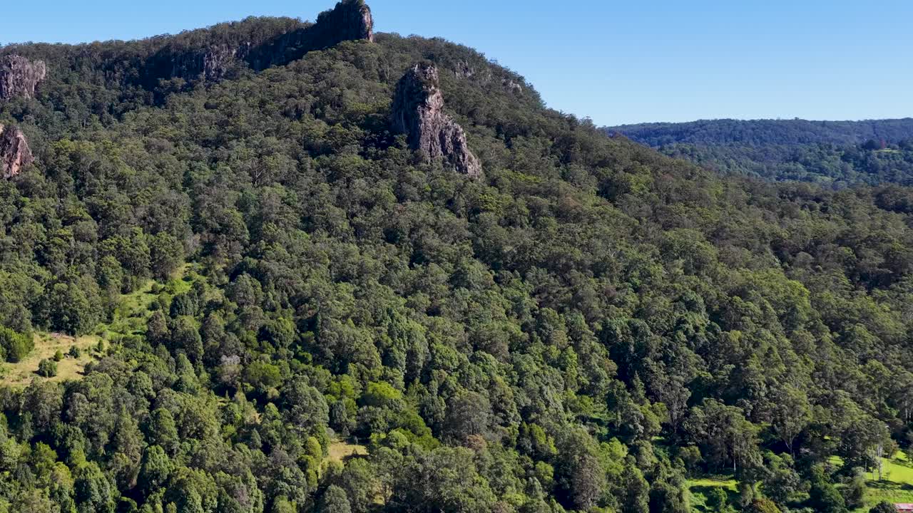 Aerial footage of lush green forest and rocky formations under clear blue skies in Nimbin, Australia