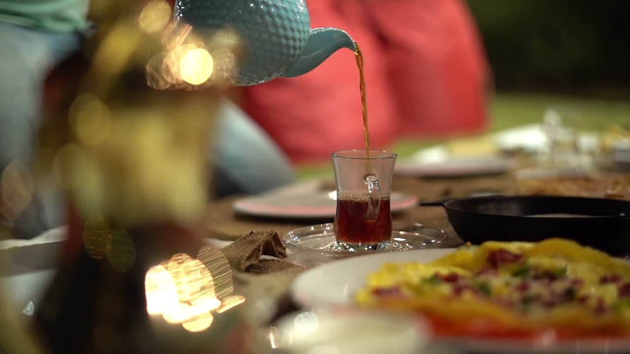 A man pours tea on a cup around Egyptian breakfast, close up shot, high angle shot, insert shot