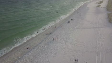 Aerial-Flight-Over-Sandy-Beach,-Waves,-And-Tourists-On-Cloudy-Day---drone-shot