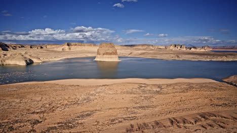 aerial footage of a massive rock standing alone in lake powell, with sweeping desert canyons stretching into the distance.