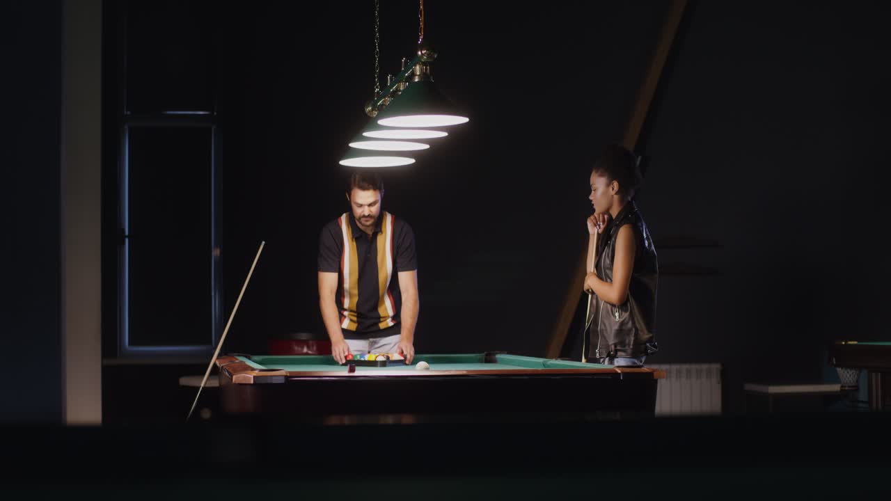 una pareja jugando al billar en un bar oscuro.