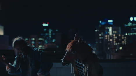 funny man wearing horse mask dancing with friends on rooftop having fun performing silly dance moves celebrating weekend together in urban city skyline