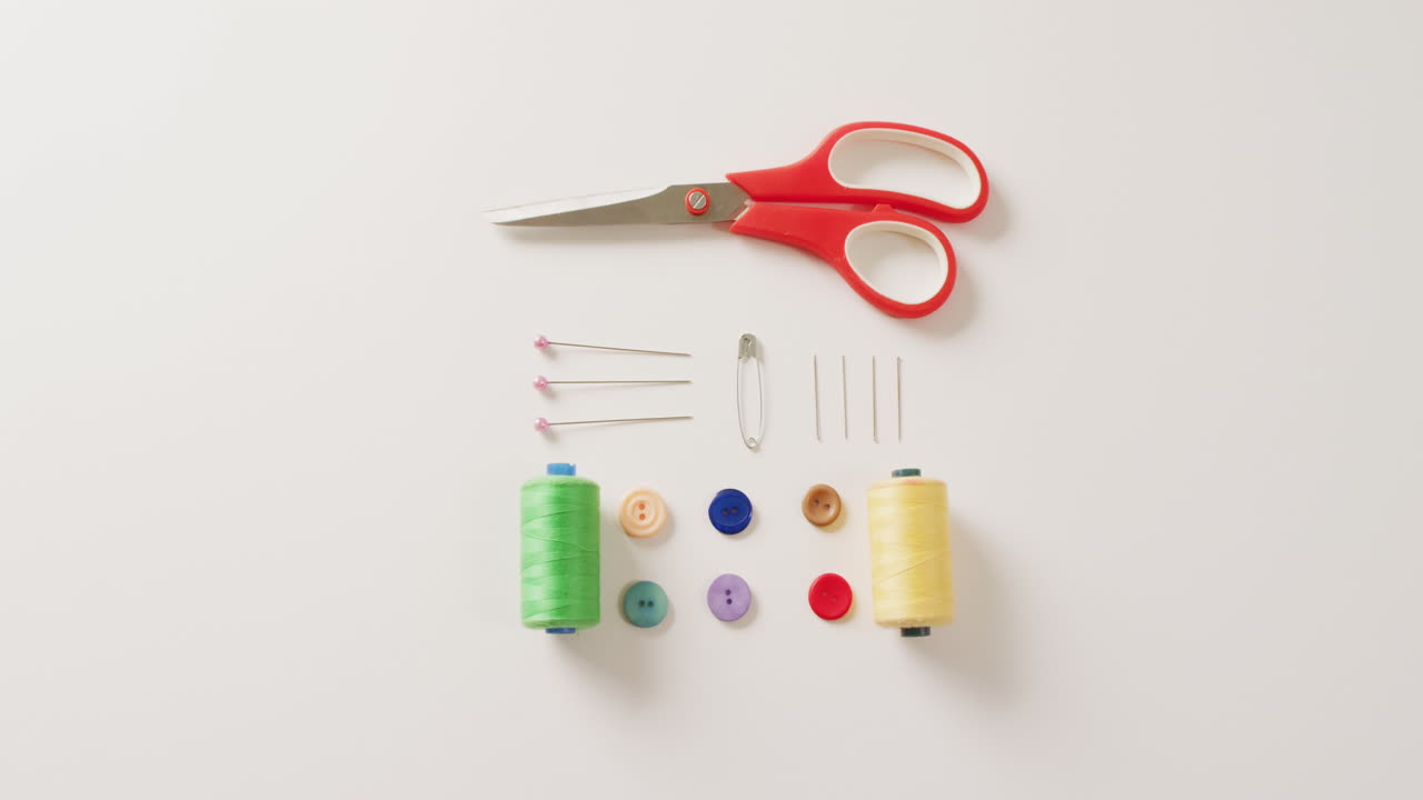 Video of scissors, buttons, pins and cotton reels arranged on white background