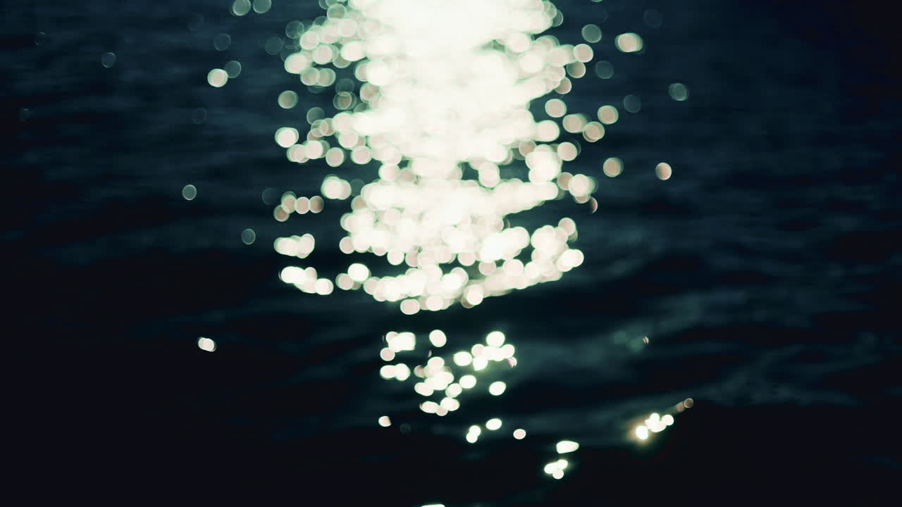 Shimmering sunlight reflects on gentle sea waves, creating bright sparkling bokeh on a deep blue water surface