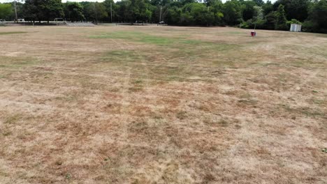 Low-drone-flight-over-a-burnt-out-grass-soccer-and-sports-fields-on-a-cloudy-summer-day