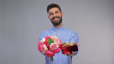 Hombre-Joven-Feliz-Con-Ramo-De-Flores-Y-Caja-De-Regalo.-Día-De-San-Valentín,-Saludo-Y-Concepto-De-Vacaciones:-Retrato-En-Video-De-Un-Joven-Feliz-Y-Sonriente-Con-Un-Ramo-De-Flores-Y-Una-Caja-De-Regalo-En-Forma-De-Corazón-Sobre-Fondo-Gris