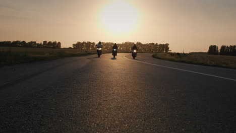 Three-bikers-drive-along-the-highway-past-the-camera