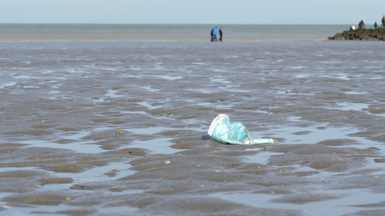 mascarilla quirúrgica usada azul tirada descuidadamente en la playa de arena de cerca