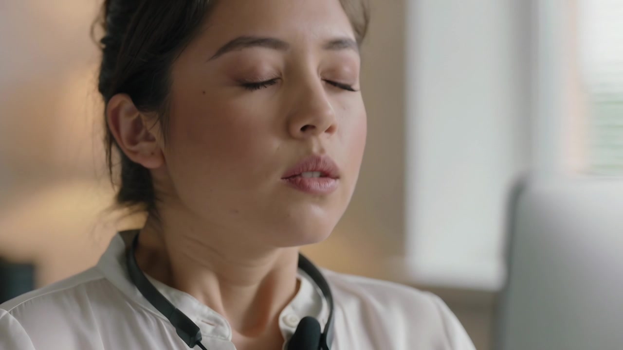 Breathing Asian woman in top with neck-device opening eyes turning gaze to screen at desk focusing