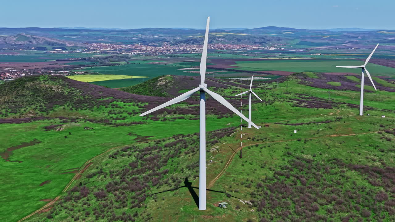 Le turbine eoliche generano energia pulita in un campo verde vicino a una città circondata da colline e terreni agricoli in una giornata di sole