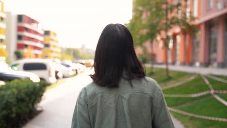 거리를 걷고 있는 아름다운 젊은 일본 여성의 뒷모습, 얼굴을 돌리고 카메라를 향해 미소를 짓고 초대의 몸짓을 하는 동안