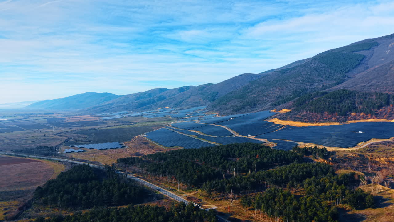 Ampio paesaggio di un impianto di energia solare in una valle di montagna. Ripresa aerea panoramica di un enorme impianto solare che si estende lungo una catena montuosa durante il giorno.