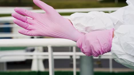 man wearing white protective suit, putting on pink latex gloves, standing on a boat