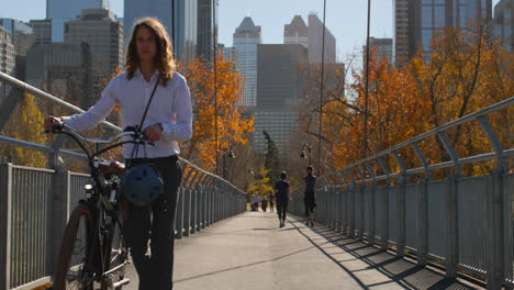 vista frontal de un joven caucásico caminando con bicicleta en el puente 4k