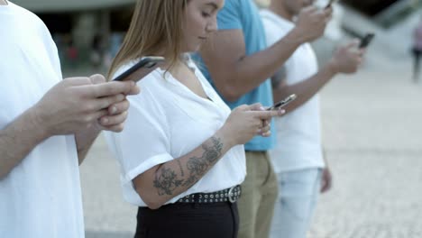 Focused-young-friends-using-smartphones-on-street