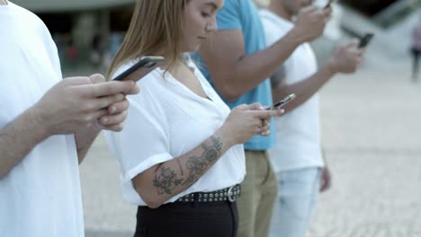 focused young friends using smartphones on street