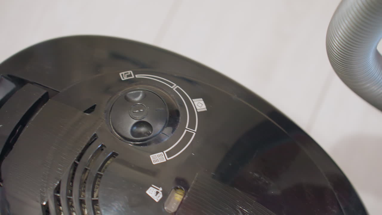 Close up view of control panel knob with printed icons on black appliance surface showing circular settings and plastic texture under soft lighting for household equipment operation and adjustment