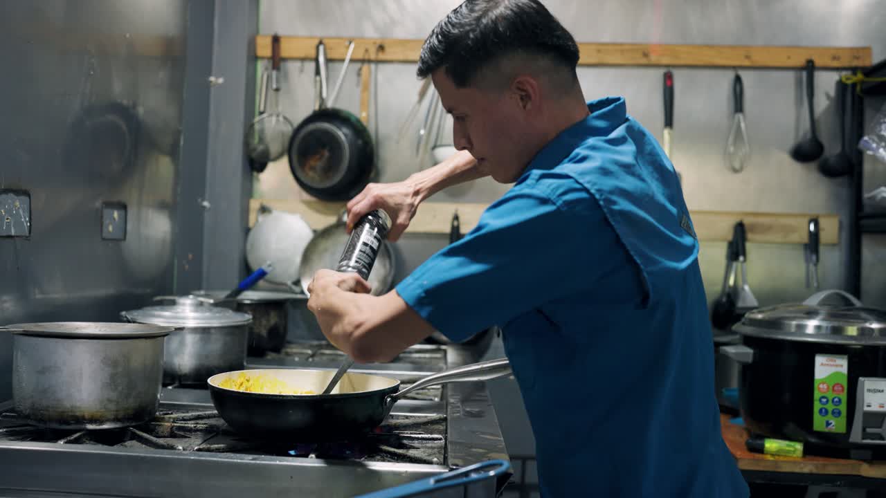 Chef che condisce il cibo con un macinapepe in una cucina commerciale.