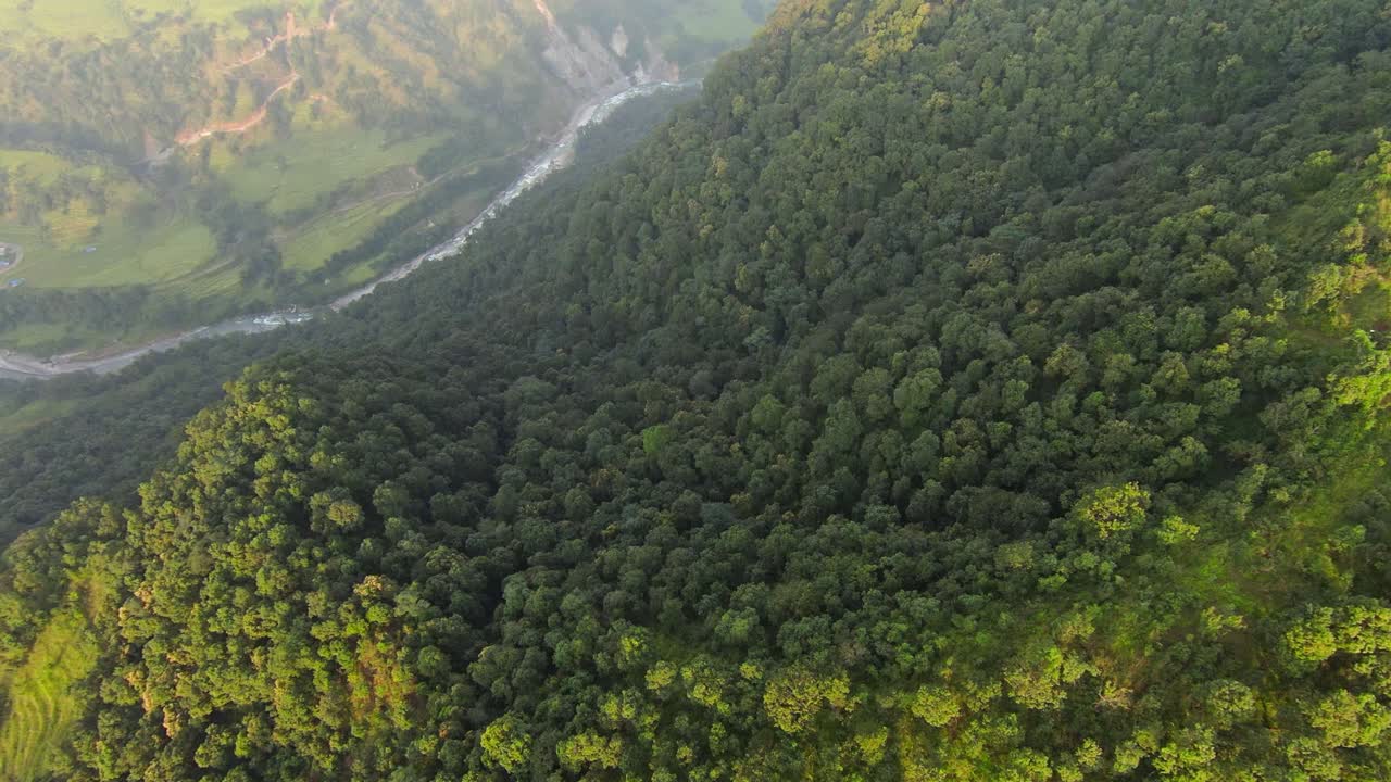 drone cinematográfico filmado sobre montañas verdes exuberantes con un río en el valle de nepal al atardecer - tiro de arriba hacia abajo