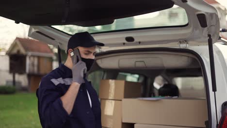 Handsome-delivery-man-checking-delivery-list-while-talking-on-the-phone.-Delivery-man-in-cap-and-gloves-with-phone-and