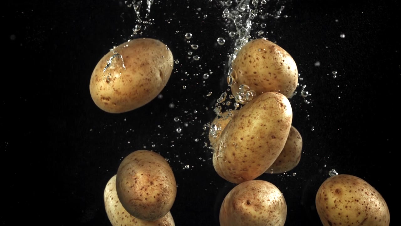 Patate fresche che cadono nell'acqua con bolle su sfondo nero.