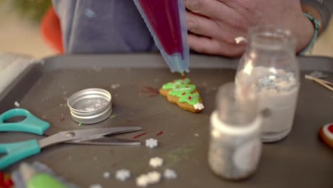 decorating a gingerbread cookie christmas tree, using a piping bag with red sugar icing