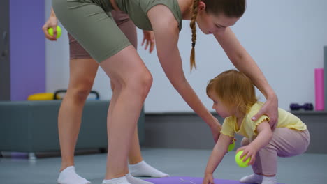 toddler interrupts gym session, crawling on mat as mother gently directs her to play, surrounded by fitness equipment and gym setting enhancing a family-friendly workout environment