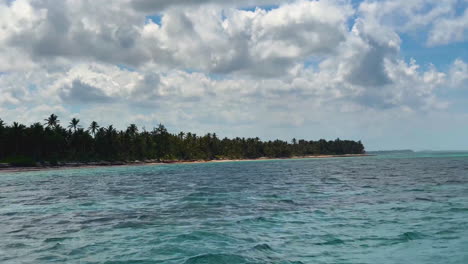 Blick-Auf-Das-Wasser-Der-Blauen-Tropischen-Karibik-Entlang-Einer-Von-Palmen-Gesäumten-Insel-In-Der-Nähe-Von-Punta-Cana,-Dominikanische-Republik,-Mit-Blauem-Himmel-Und-Geschwollenen-Wolken