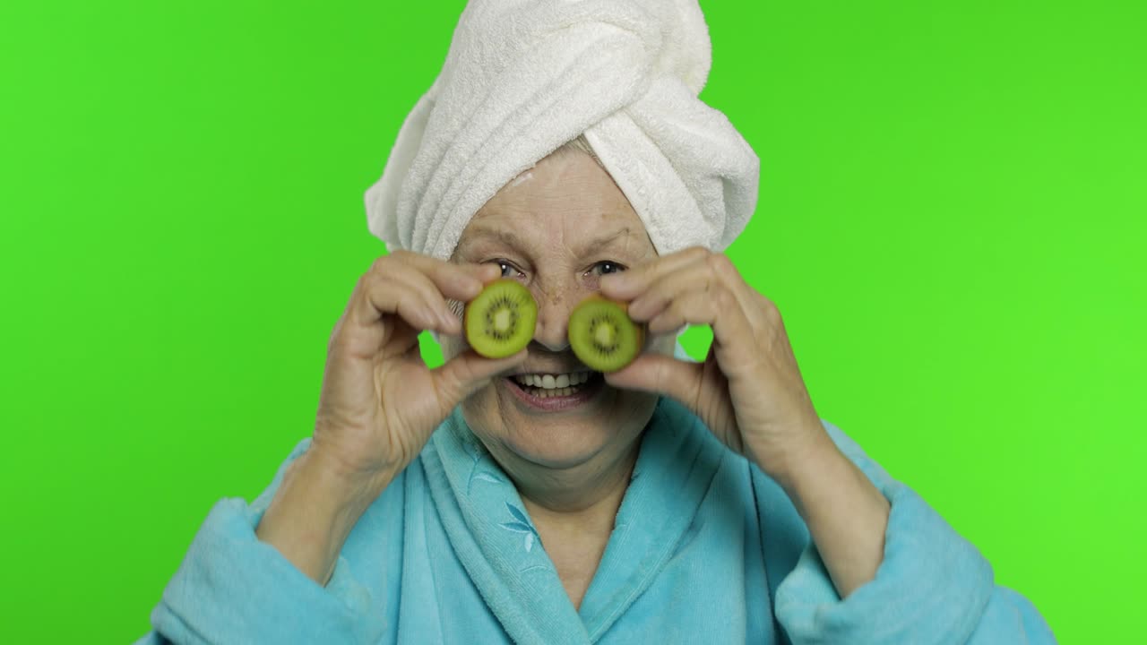 abuela anciana en bata de baño después de la ducha. anciana con dos mitades de kiwi