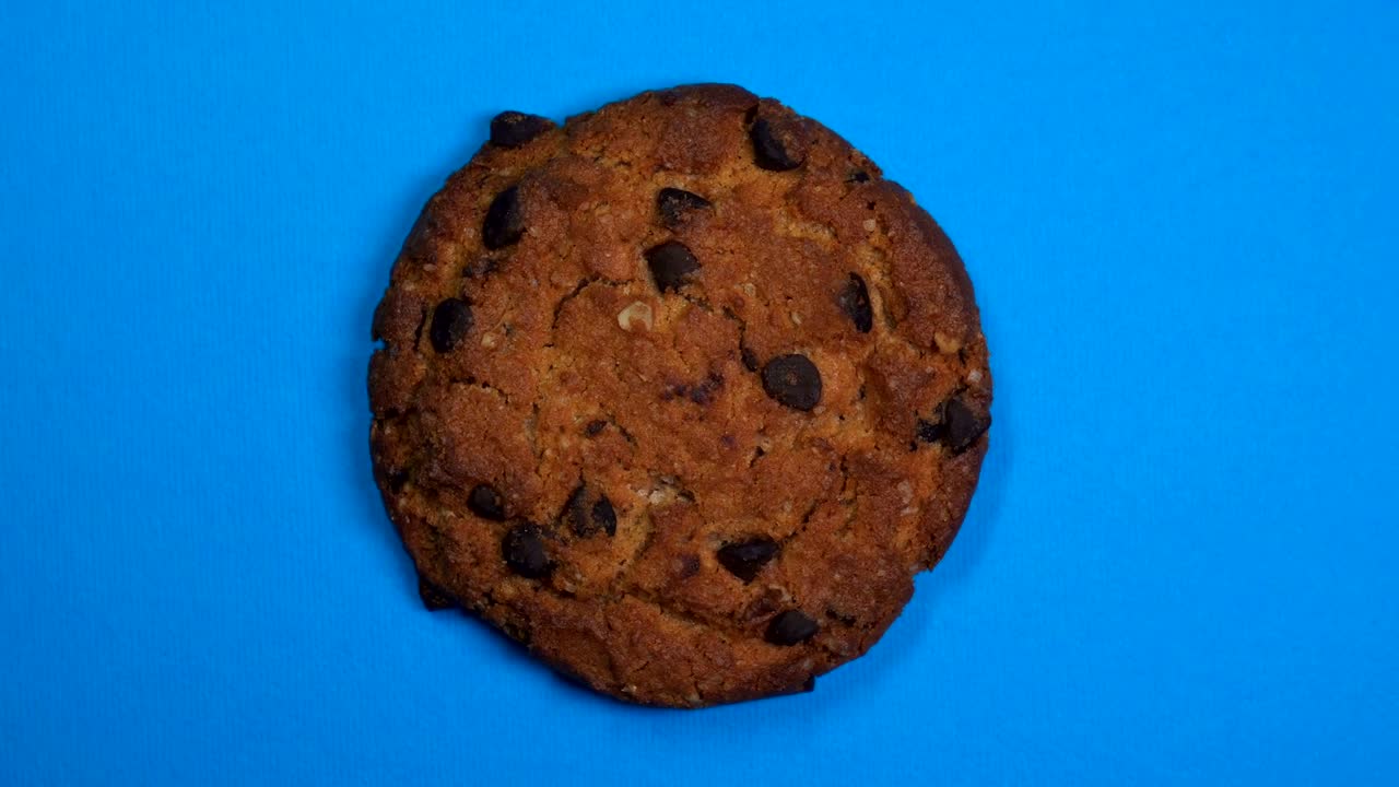 Chocolate chip cookie close-up, macro shot, fast spinning on a rotating blue background.