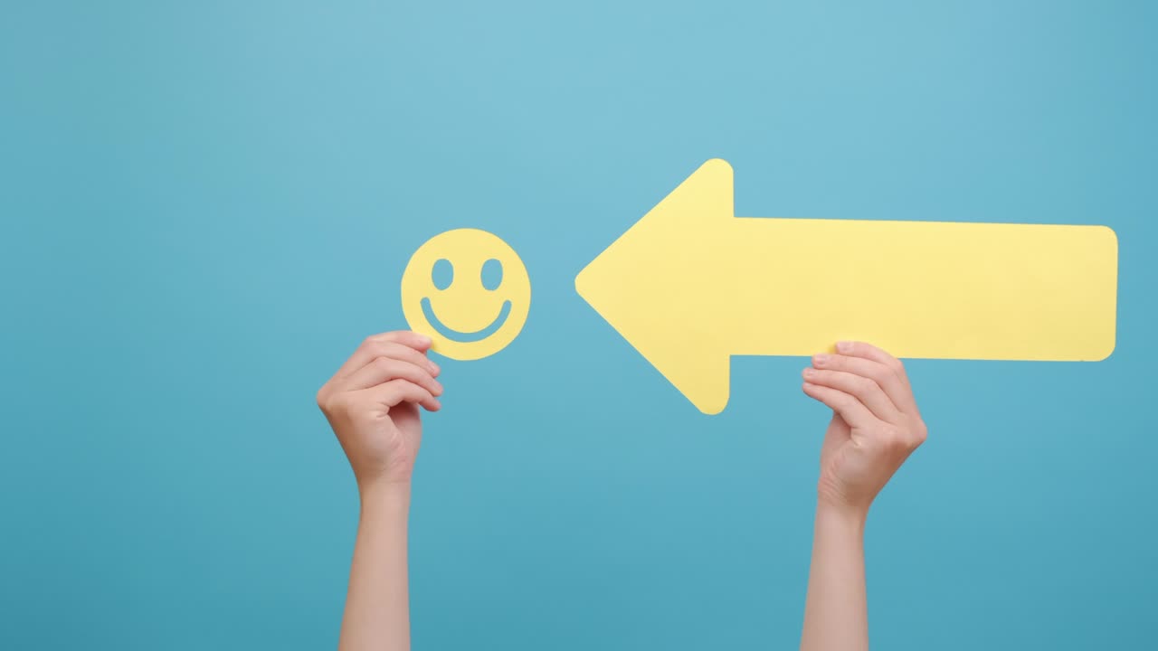 노란색의 행복한 웃는 얼굴과 큰 화살표를 들고있는 여성 손의 근접, 복사 공간과 함께 파란색 배경 벽에 고립되어 있습니다. 개념 트렌드, 따르는 리더, 고객 만족 또는 피드백