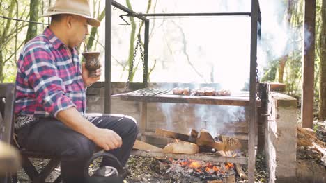 ethnic man drinking mate against barbecue rack in garden