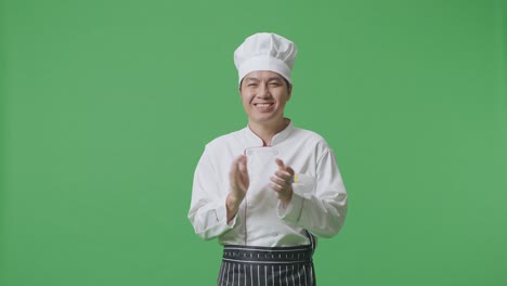 el chef asiático sonriendo y aplaudiendo sus manos mientras está de pie en el estudio de fondo de la pantalla verde