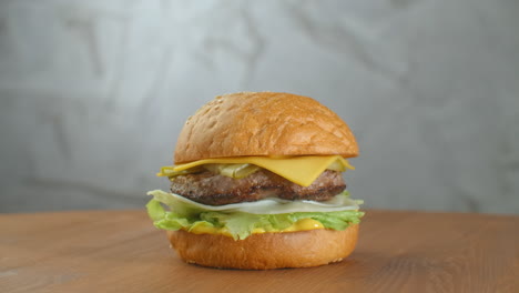 Great-Burger-with-beef-cutlet-tomatoes-mushrooms-and-cucumbers-with-melted-cheese-rotates-on-a-wooden-Board-on-light-background.