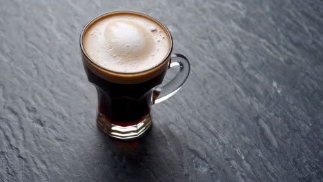 close-up of a glass mug of espresso on a dark stone surface