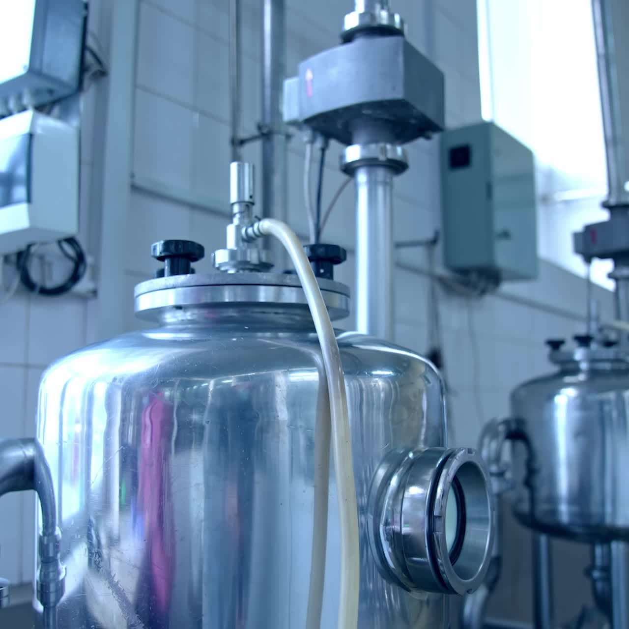 Two small cisterns with the adjusted pipes and tubes. Metal reservoirs placed in front of the window at the milk factory. Close up