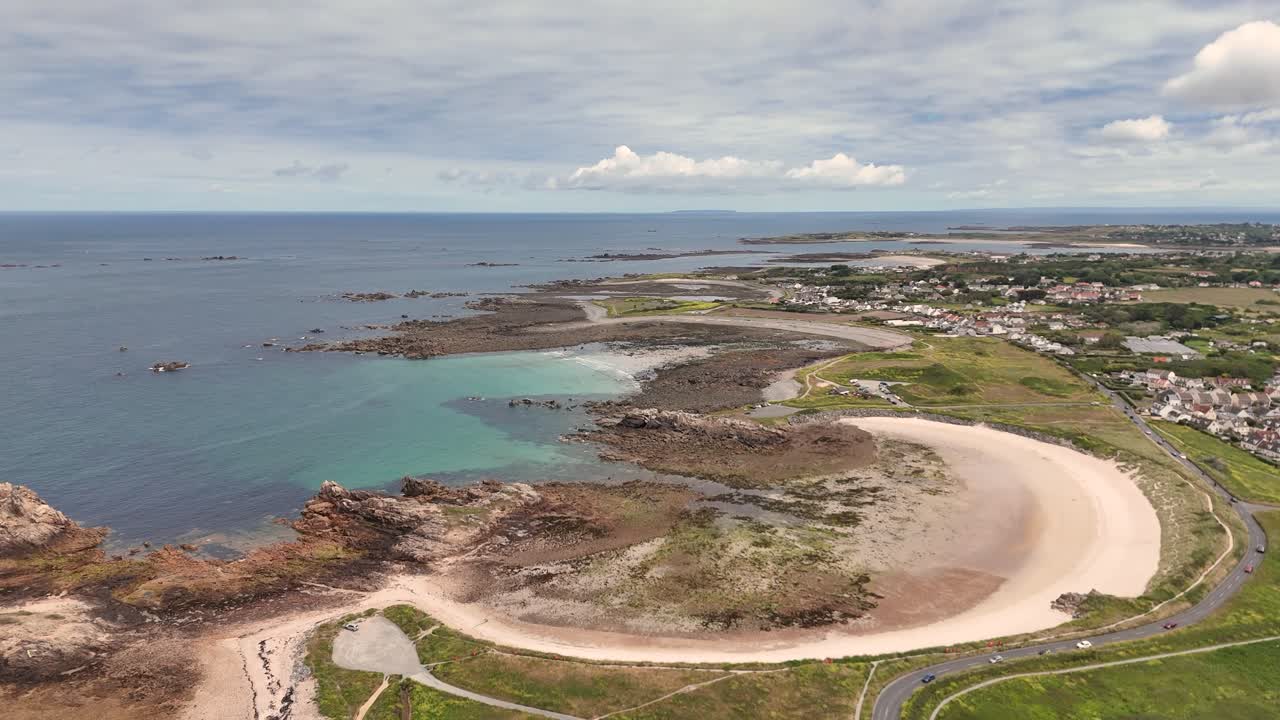 Guernsey.High drone flight over beautiful bay with golden beach on West coast of Guernsey with calm clear turquoise sea and rocky foreshore on bright sunny day
