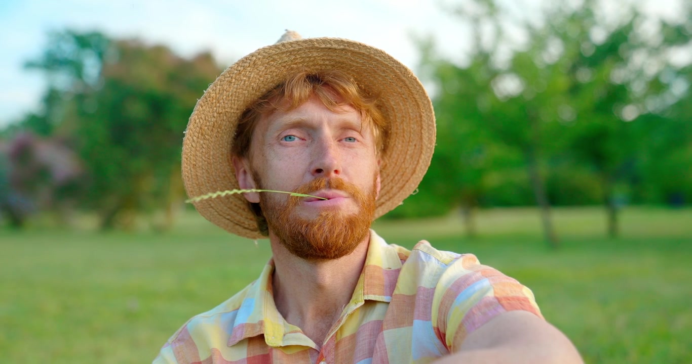 Thoughtful Man with Red Beard and Straw Hat Chewing Grass in a Field