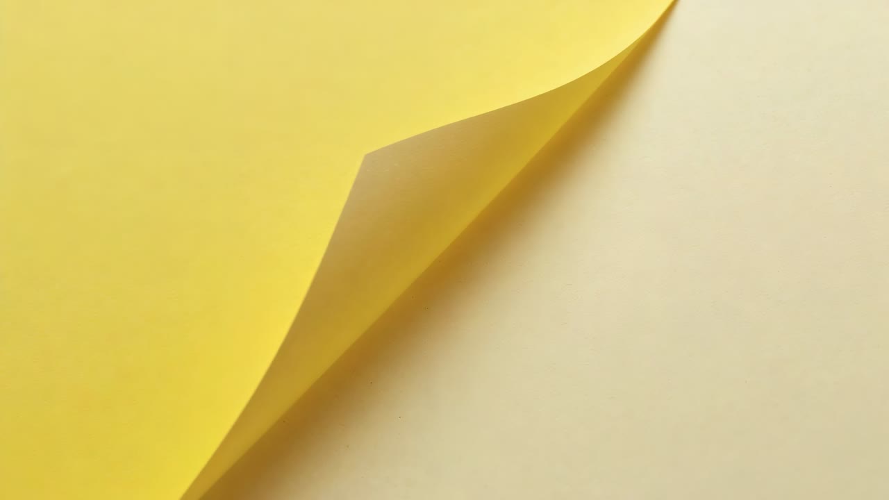 Top-right corner lifting, peeling yellow paper sheet revealing pale-beige sheet beneath on tabletop