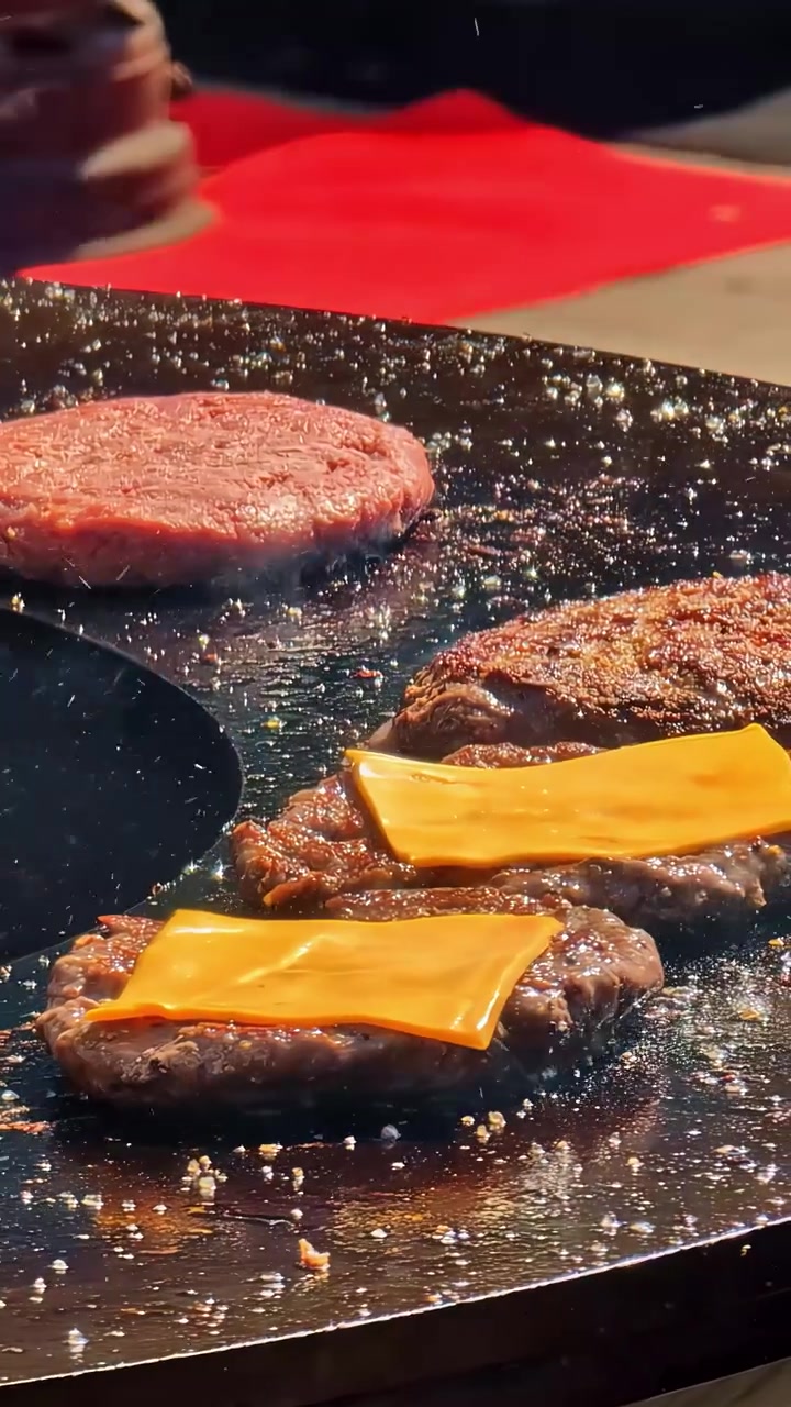 Hamburger succulenti con fette di formaggio che si sciolgono su una griglia mentre le fiamme tremolano. Adatto per pubblicità alimentare o dimostrazioni culinarie.