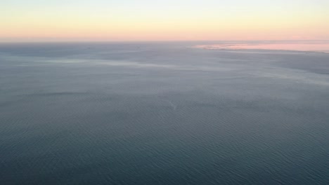 aerial tilt up from turquoise water sea to beautiful golden hour horizon during sunset