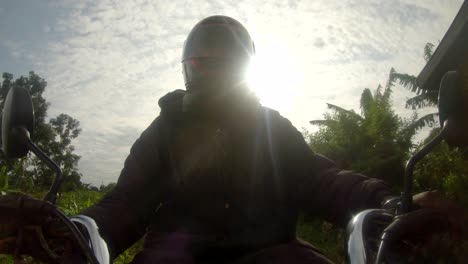 a action shot of an african man wearing a helmet while steering a motor bikes handle bars rides through rural africa with the sun shining behind