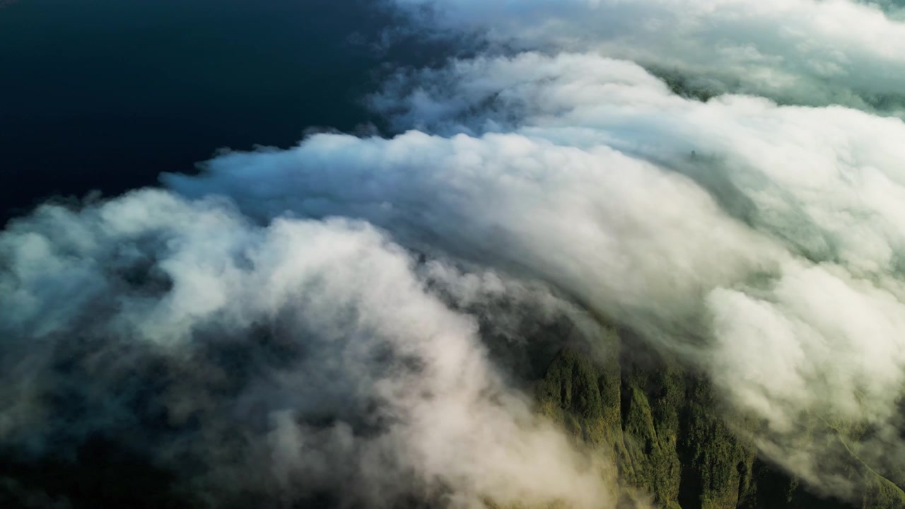 Luftaufnahme: Ziehende Wolken über einem Gebirgskamm mit schnell bewegender Wolkendecke über üppig grünen Hängen, die eine dramatische atmosphärische Landschaft und dynamisches Wetter erzeugen.